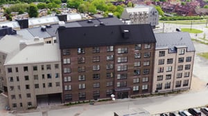 Flerfamiljshus med fasader i olika nyanser av brunt och grått, omgiven av grönska och parkeringsplatser