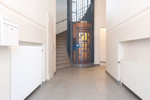 Entréområde med trapphus, hiss med glasdörrar, brevlåda och element på väggarna