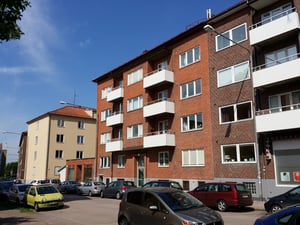 Flerbostadshus i tegel med vita balkonger, parkerade bilar på gatan och klarblå himmel