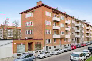 Flerfamiljshus i tegel med balkonger, parkerade bilar längs gatan och en klar himmel i bakgrunden