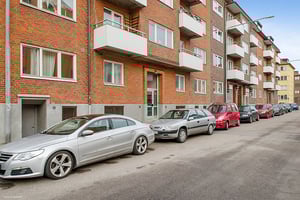 Flerfamiljshus i tegel med balkonger och parkerade bilar längs en gata