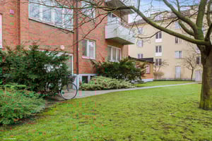 Flerbostadshus i tegel med grönskande trädgård, gräsmatta och en cykel vid sidan