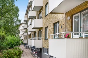 Lägenhetsbyggnad med tegelväggar, vita balkonger och cyklar parkerade längs en gångväg omgiven av grönska