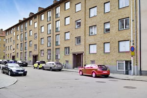 Flerfamiljshus med fasad av gul tegel, parkerade bilar längs gatan och en cykel vid entrén