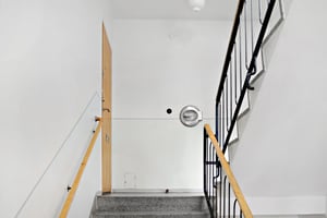 Trappa med grå stentrappsteg, svarta och träfärgade räcken, en träfärgad dörr samt vitmålade väggar