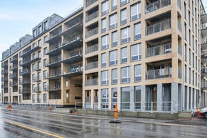 Modernt flerfamiljshus med fasad av tegel, stora fönster och balkonger, beläget vid en våt asfalterad gata