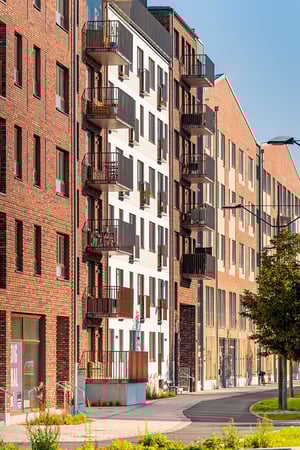 Flerbostadshus med fasader av tegel och ljus puts, balkonger och stora fönster, längs en gångväg med grönska