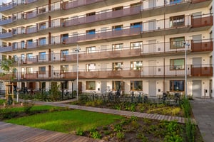 Flerfamiljshus med flera balkonger, en grön innergård och cykelställ i förgrunden