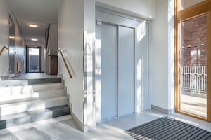 Entréområde med trappor, hiss och glasdörrar som släpper in naturligt ljus från utsidan