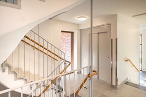 Trappa med metallräcke och ljusa väggar vid sidan av en hiss i ett modernt trapphus