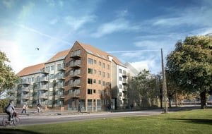 Nybyggnad med flerfamiljshus i tegel och ljusa fasader, omgiven av grönska och en cyklist på en gata i förgrunden