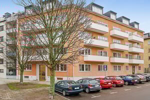 Bostadshus med orange fasad, vita balkonger och fem våningar, parkerade bilar framför byggnaden på en asfalterad gata