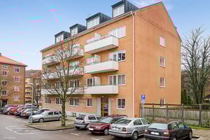 Lägenhetsbyggnad i flera våningar med orange fasad, balkonger och parkeringsplatser framför