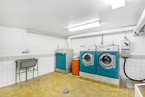 Tvättstuga med två tvättmaskiner, en torktumlare, vask och gult klinkergolv