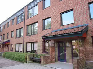 Flerfamiljshus i rött tegel med flera våningar, stora fönster och en entrédörr med tak