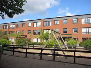 Radhus i tegel med tre våningar, lekplats med gungställning och sandlåda i förgrunden