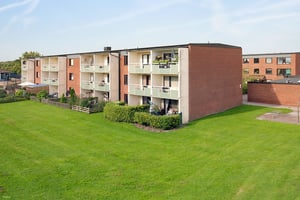 Flerfamiljshus med röda tegelväggar och balkonger, omgivna av en grön gräsmatta under en klar blå himmel