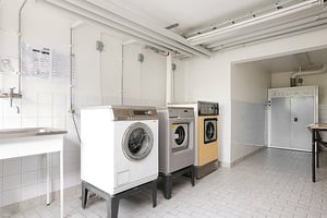 Tvättstuga med flera tvättmaskiner, torktumlare och ett tvättställ på klinkergolv
