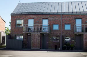 Radhus med tegelfasad, balkonger, och grå dörrar på en solig dag