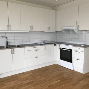 Vitt kök med skåp, spis, fläkt, diskho och bänkskiva, samt ljust trägolv