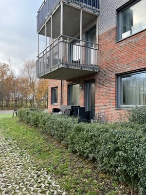 Flerfamiljshus i tegel med balkonger, fönster och en uteplats omgiven av gröna buskar