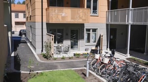 Modernt flerfamiljshus med balkonger, innergård med cykelställ, grön gräsmatta och sittplatser utomhus