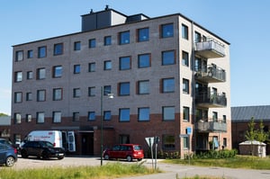 Flerfamiljshus med fem våningar, fasad av tegel och puts, parkeringsplats med bilar och en grön omgivning