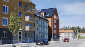 Flerfamiljshus i olika färger längs en lugn gata med parkerade bilar och träd i förgrunden