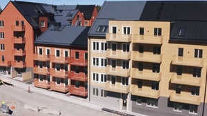 Flerfamiljshus med färgglada fasader i orange, gult och beige samt balkonger, belägna vid en gata under konstruktion