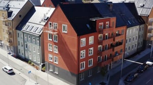 Flerbostadshus med fasader i olika färger, inklusive rött och grått, vid en gata med parkerade bilar och träd