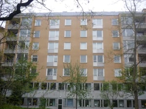 Gul flerfamiljsbyggnad med sex våningar, omgiven av träd och buskar