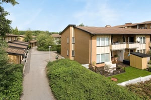 Flerfamiljshus i tegel med balkonger och trädgårdar, omgivna av grönska och en asfalterad gångväg