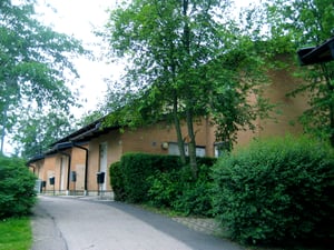 Radhus byggda i tegel, omgivna av grönskande träd och buskar, med en gångstig som leder fram till byggnaderna