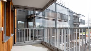 Modern lägenhetsbalkong med glasräcken och utsikt över en byggnad med mörka fasader