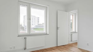 Inflyttningsklart rum med vita väggar, parkettgolv och ett fönster med utsikt över moderna byggnader