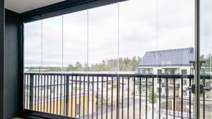 Balkong med glasräcke och utsikt över ett bostadsområde med moderna byggnader och träd i bakgrunden