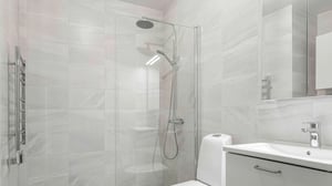 Modern badrum med ljusa kakelväggar, glasduschvägg, takdusch, vit kommod och spegel med förvaring