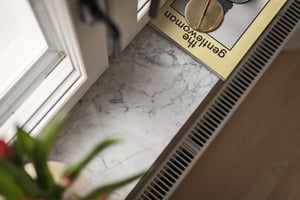 Fönsterbräda i vit marmor med ett mynt och en tidning delvis synliga, bredvid ett ventilationsgaller