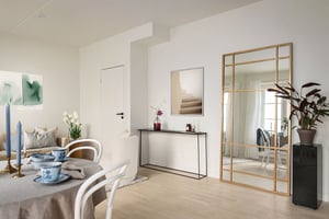 Ljust och modernt vardagsrum med matplats, spegel med guldram, konsolbord med dekorationer, och växter