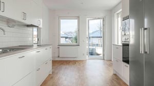 Modernt kök med vita skåpluckor, träparkettgolv och stora fönster som släpper in naturligt ljus