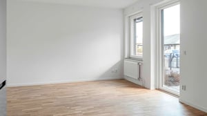 Inflyttningsklart rum med parkettgolv, vitmålade väggar och stora fönster som släpper in mycket dagsljus