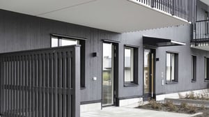 Modern flerfamiljshus med mörkgrå fasad, stora fönster, och ingång med överhängande tak