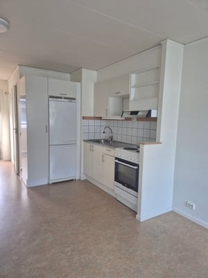 Ljus kök med vit inredning, kylskåp, ugn, spis och diskho. Laminatgolv och vitmålade väggar