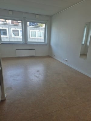 Inflyttningsklart rum med ljust trägolv, vita väggar och stora fönster som släpper in naturligt ljus