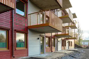 Flerfamiljshus med träfasad i rött och grått, stora fönster och balkonger med orange räcken