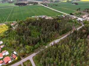 Landskapsvy med en skog omgiven av åkrar, bostadsområden och små vägar