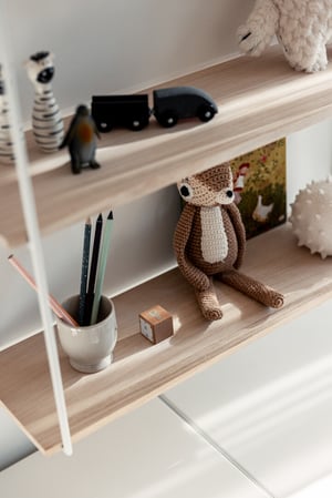 Trähylla med en mjukstickad leksak, en vit mugg med pennor, små svarta leksaksbilar och ett kort med ett motiv av en anka