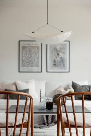 Modern inredning med ljusa trästolar, ett bord med dekor och en soffa med kuddar framför två inramade konstbilder på väggen