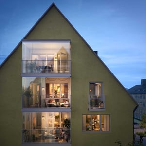 Ett modernt flerfamiljshus med gul fasad, stora glasbalkonger och interiör som lyser upp på kvällen