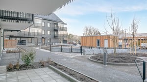 Modern lägenhetskomplex med en innergård som har gångvägar, träd och cykelställ, omgivna av byggnader och träfasader under en klar himmel